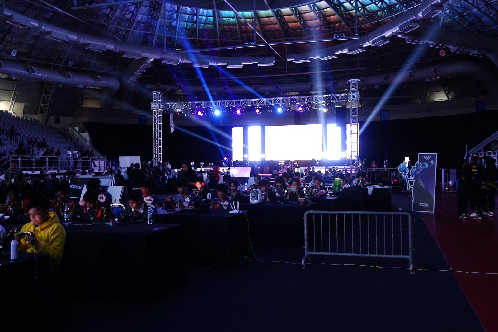A lively community game-night crowd filling a big arena with a lit stage